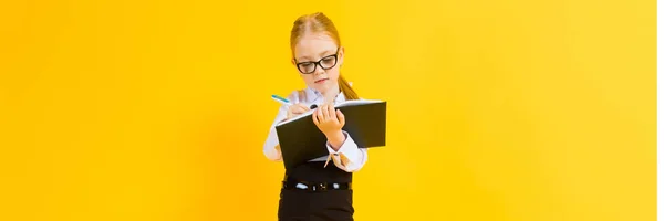 Девушка с рыжими волосами на желтом фоне. Очаровательная девушка в прозрачных очках пишет ручку в блокноте . — стоковое фото