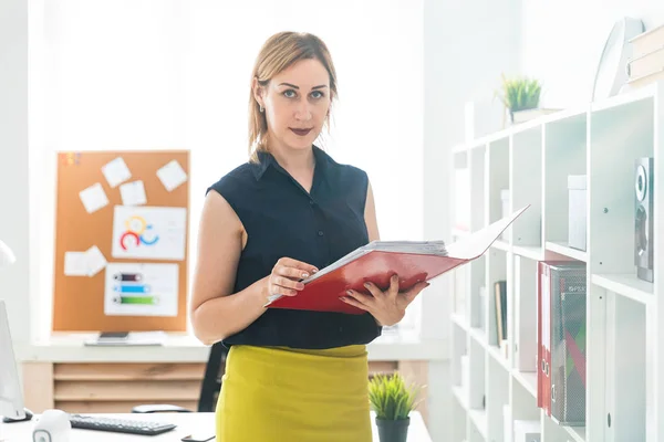 En ung flicka stående på kontoret och hålla en mapp med dokument. — Stockfoto