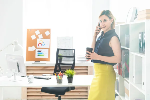 Een jong meisje praten aan de telefoon bij het kantoor en houd een glas van koffie. — Stockfoto