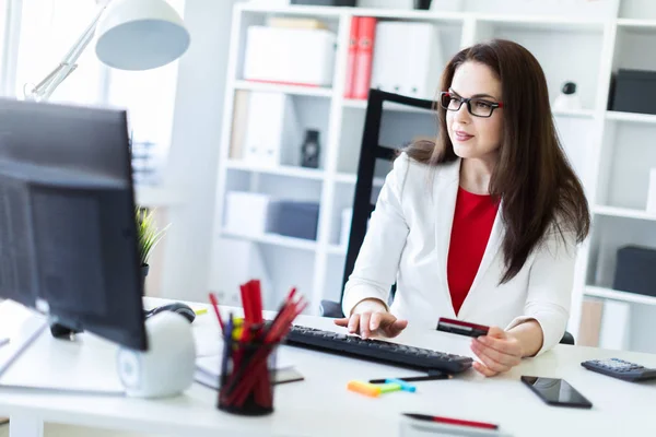 Een jong meisje in het Bureau aan de tafel zitten en houden van een bankkaart. — Stockfoto