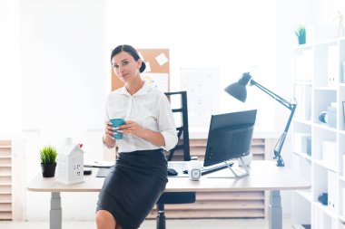 Ofiste duran ve bir fincan tutan genç bir kız.