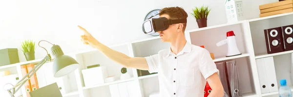 Um jovem de óculos de realidade virtual fica perto da mesa e puxa o braço para cima. Um jovem polegar uma página virtual . — Fotografia de Stock