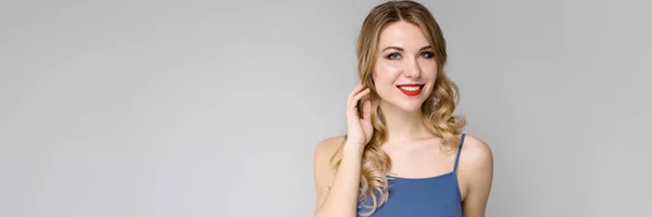 Menina encantadora com cabelo encaracolado longo branco. Menina em um top azul e calças azuis no fundo cinza — Fotografia de Stock