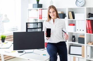 Masaya oturdu ve bir telefon ve bir banka kartı tutan genç bir kız.