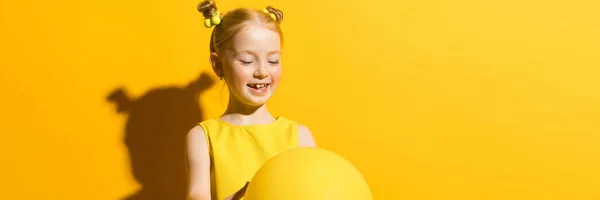 Ragazza con i capelli rossi su sfondo giallo. La ragazza si tiene tra le mani e guarda il palloncino giallo . — Foto Stock