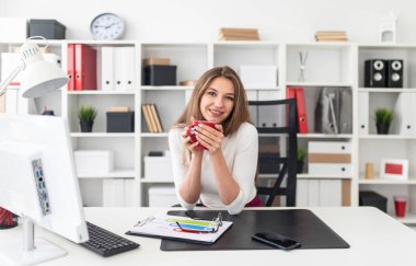 Ofiste bir masada oturan ve bir kırmızı Kupası tutan genç bir kız.