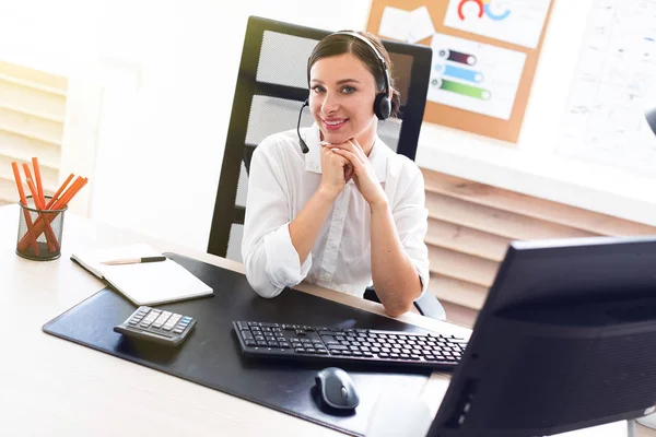 Una joven en auriculares con un micrófono sentado en una mesa de ordenador . — Foto de Stock