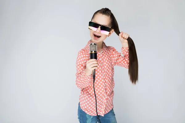 Menina em um fundo cinza cantando no microfone . — Fotografia de Stock