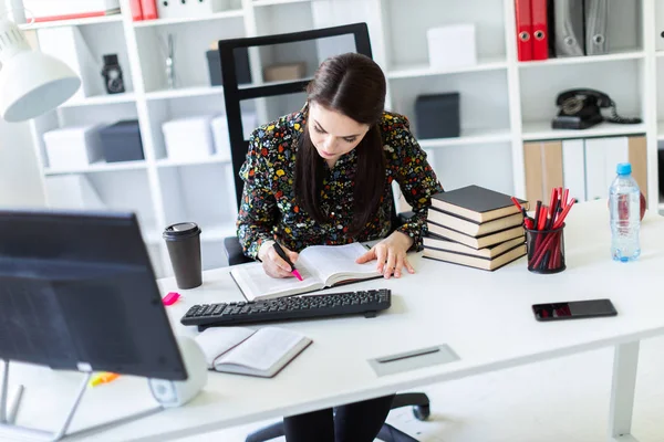 En ung flicka sitter på kontoret på datorn skrivbord och arbetar med en bok. — Stockfoto