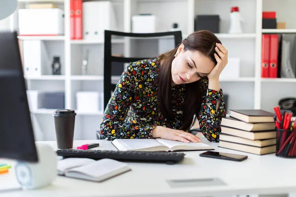 Una joven sentada en la oficina en el escritorio de la computadora y trabajando con un libro . — Foto de Stock