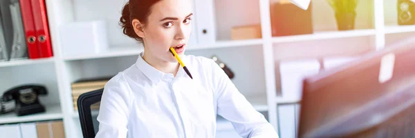 Una giovane ragazza in ufficio tiene una penna in bocca e lavora con una calcolatrice, documenti e un computer . — Foto Stock
