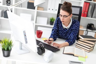 Bir genç kız bardaklarda Office masada oturur ve klavyede yazdırır.