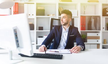 Genç bir adam bir bilgisayar Resepsiyon ofiste oturan ve belgeleriyle çalışma.