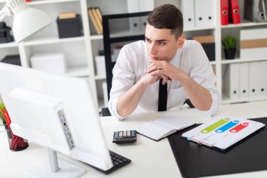Genç bir adam bir bilgisayarda ofis masasında oturan ve belgeleriyle çalışma.