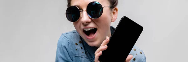 Jeune fille brune en lunettes rondes. Les cheveux sont rassemblés dans un chignon. Fille avec un téléphone noir . — Photo
