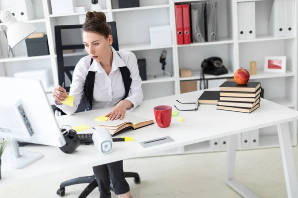 Молодая девушка сидит за столом в офисе, держит карандаш и работает со стикерами . — стоковое фото
