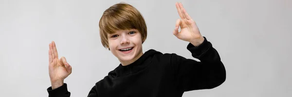 Portrait of adorable little happy smiling boy standing in studio showing ok sign on grey background — Stock Photo, Image