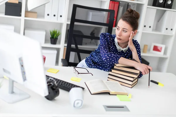 Genç bir kız bilgisayar masası ofisinde oturuyor, bir yığın kitap üzerinde eğilir ve ekrana görünüyor.
