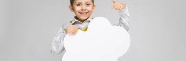 Beyaz bir gömlek, çizgili kolsuz bluz ve ışık kot büyüleyici bir çocuk gri bir arka plan üzerinde duruyor. Çocuk beyaz bir poster bir bulut şeklinde düzenliyor