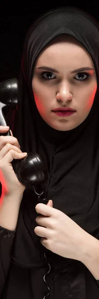 Retrato de hermosa mujer musulmana asustada seria joven usando hijab negro sosteniendo el teléfono para llamar como concepto de elección sobre fondo negro — Foto de Stock