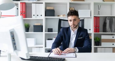 Genç bir adam bir bilgisayar Resepsiyon ofiste oturan ve belgeleriyle çalışma.