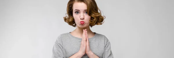 Charmante jonge meisje in een grijs T-shirt op een grijze achtergrond. Het meisje haar handen opgevouwen — Stockfoto