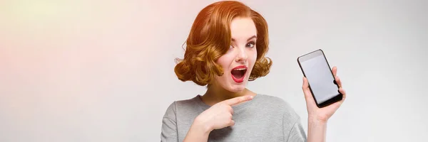 Encantadora joven con una camiseta gris sobre un fondo gris. Una chica sostiene un teléfono en su mano — Foto de Stock