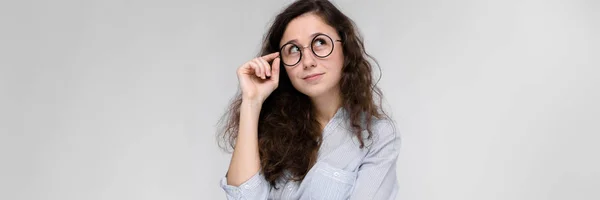 Retrato de una joven con gafas. Hermosa joven sobre un fondo gris. Una joven con una blusa clara y pantalones oscuros . —  Fotos de Stock