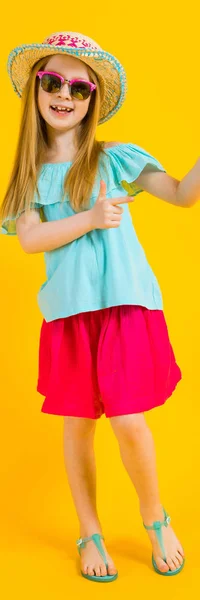 Chica con el pelo rojo sobre un fondo amarillo. Una chica encantadora con ropa de verano brillante señala sus dedos hacia un lado . —  Fotos de Stock