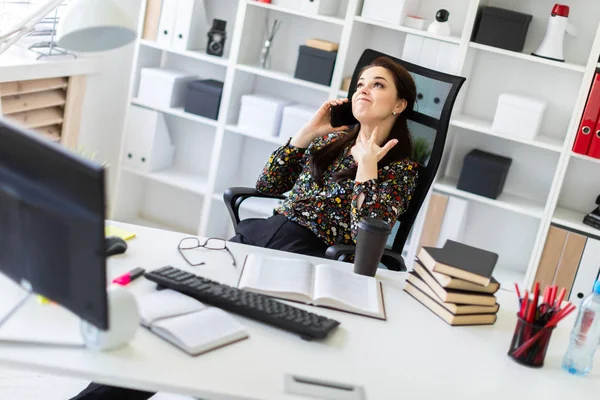 Una joven sentada en la oficina en el escritorio de la computadora y hablando por teléfono . — Foto de Stock