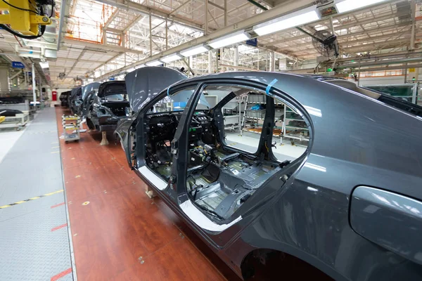 Añadir detalles a la carrocería del coche. El equipo robótico hace el montaje del coche. Asamblea de coche moderno en fábrica —  Fotos de Stock