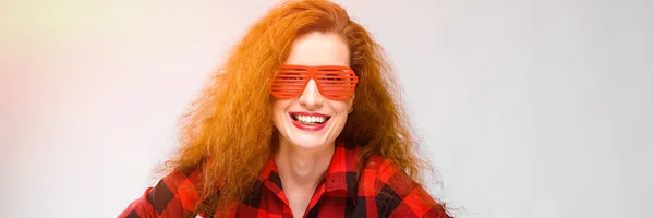 Portrait de belle rousse heureuse jeune femme en lunettes souriant tenant la main sur sa taille sur fond gris — Photo