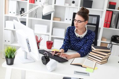 Bir genç kız bardaklarda Office masada oturur ve klavyede yazdırır.