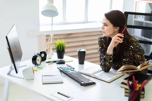 Een jong meisje zittend op kantoor op de computer Desk en het werken met een boek. — Stockfoto