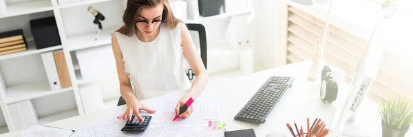 Una joven en la oficina lleva un marcador rosa en la mano y cuenta con una calculadora . — Foto de Stock