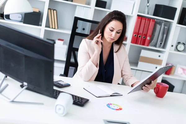 Een jong meisje zitten achter een computer bureau, holding van een pen en werken met een grafiek en een computer. — Stockfoto