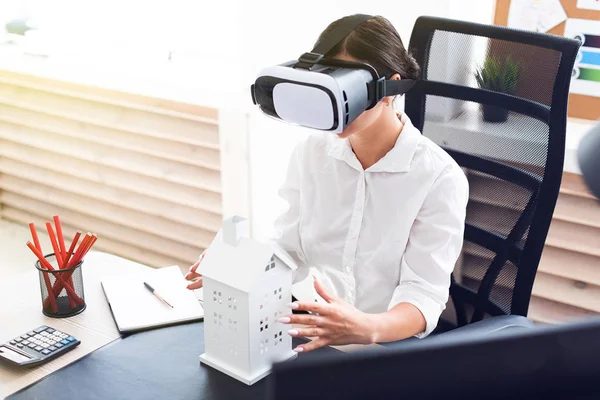 Young girl sitting in virtual reality glasses. Before her on the table is the layout of the house.