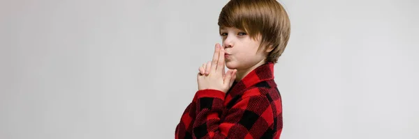 Cute confident funny little caucasian boy in checkered shirt making pistol with his hands on grey background — Stock Photo, Image