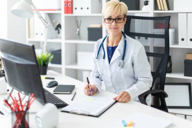Masada oturan ve bir kalem tutan beyaz bir elbise içinde bir genç kız.