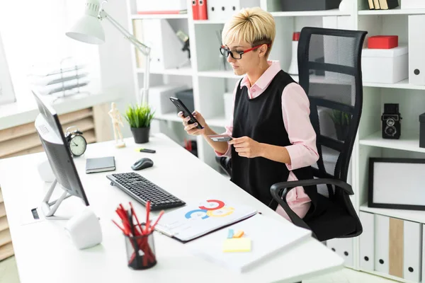 Una ragazza seduta alla scrivania di un computer con in mano un telefono e una carta bancaria . — Foto Stock