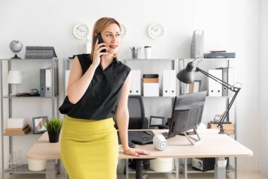 Bir genç kız ofiste ayakta ve telefonda konuşurken.