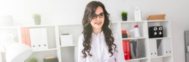 Güzel genç kız Ofis Masası duruyor ve onun elinde tutan bir kalem ve bir hesap makinesi.