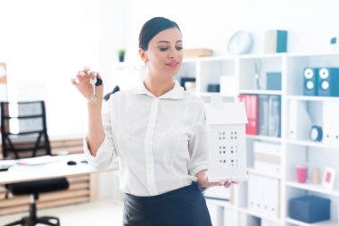 Genç bir kız ofiste ayakta ve tutmak belgili tanımlık anahtar taşı ve evin düzeni.