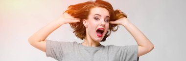Gri T-shirt gri bir arka plan üzerine sevimli genç kız. Kız onun baş ve çığlıklar arkasında ellerini tutar