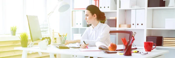 Una giovane ragazza in ufficio tiene in mano un pennarello rosa e lavora con un computer e documenti . — Foto Stock