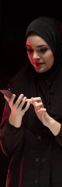 美しい正フレンドリーな若いイスラム教徒女性の黒い背景に携帯電話を保持している黒のヒジャーブを身に着けている肖像画 — ストック写真
