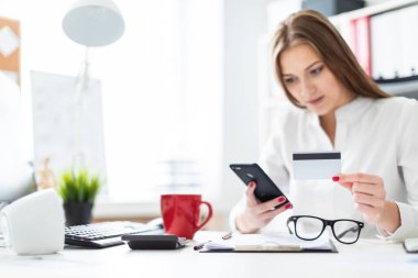 Office masada oturan ve bir telefon ve bir banka kartı tutan genç bir kız.