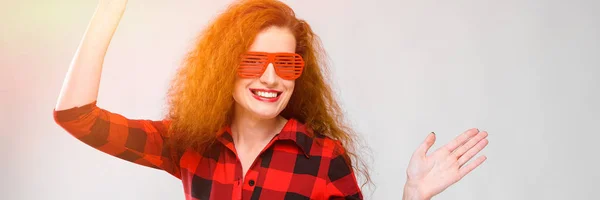 Menina ruiva jovem em uma camisa quadriculada vermelha. Menina encantadora em óculos vermelhos. Menina dançando — Fotografia de Stock