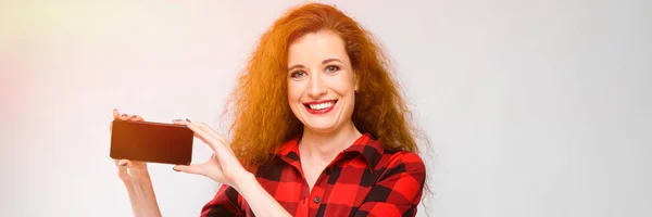 Young red-haired girl in a red checkered shirt. Young girl holding a phone — Stock Photo, Image