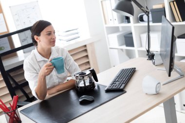 Ofiste bir masada oturan ve bir fincan tutan genç bir kız.